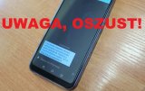 zdjęcie kolorowe, z dużym, czerwonym napisem UWAGA, OSZUST!. na zdjęciu telefon komórkowy z wiadomością SMS