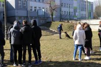 zdjęcie kolorowe, między uczniami patrzącymi w kierunku szkoły widać przewodnika psa służbowego z psem