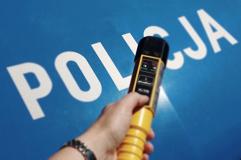 Na masce samochodu z napisem Policja na niebieskim tle widać wyciągniętą dłoń trzymającą urządzenie do badania stanu trzeźwości
