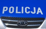 Na zdjęciu widać przód maski policyjnego radiowozu marki KIA. maska w kolorze srebrnym i niebieskim z srebrnym napisem pośrodku POLICJA