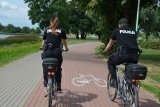 Na kolorowym zdjęciu widoczny jest patrol policji na rowerach, jadący po ścieżce rowerowej