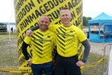 Na zdjęciu widoczni dwaj policjanci ubrani w żółte koszulki sportowe z napisem RUNMAGEDDON. Obaj są uśmiechnięci, za nimi żółty owalny balon z napisem RUNMAGEDDON.