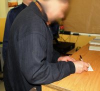 Podejrzany podpalacz podpisuje dokumenty w Pomieszczeniu Osób Zatrzymanych