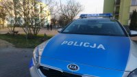 Na pierwszym planie, w prawym rogu radiowóz policyjny. W tle policjanci w trakcie patrolu ulicami miasta Sokółka.
