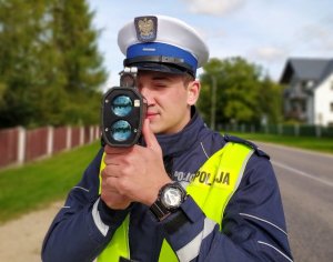 Policjant ruchu drogowego wykonuje pomiar prędkości za pomocą ręcznego miernika.