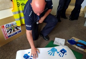 policjant odbijający dłoń zanurzoną w niebieskiej farbie na białej kartce papieru