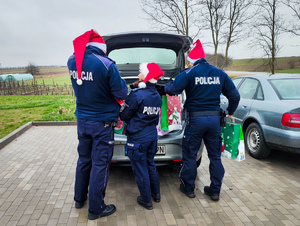 Policjanci wyjmują z samochodu prezenty.