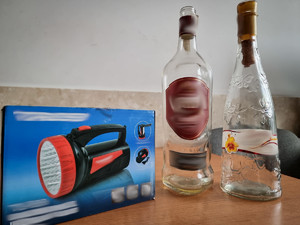Dwie puste butelki po alkoholu i latarka ustawione na stole.