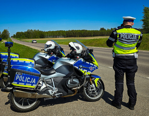 Policjant motocyklista mierzy prędkość jadących pojazdów, obok motocykle.