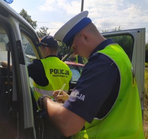 Policjant Wydziału Ruchu Drogowego w trakcie wypełnia dokumentację związaną z kolizją drogową.