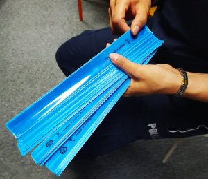 Policjantka zespołu ds. prewencji kryminalnej rozdaje uczestnikom półkolonii elementy odblaskowe.