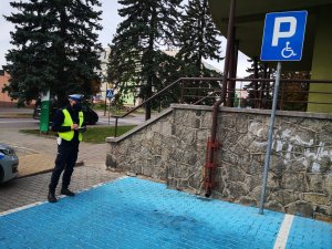 Policjant kontroluje miejsce parkingowe dla niepełnosprawnych oznaczone niebieską barwą i znakiem pionowym.