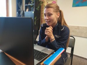 Policjantka prowadzi lekcje za pomocą komunikatora internetowego. Siedzi przed laptopem, w tle wnętrze pokoju zespołu ds. patologii nieletnich.
