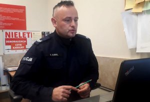 policjant siedzący przed laptopem prowadzi zajęcia online.