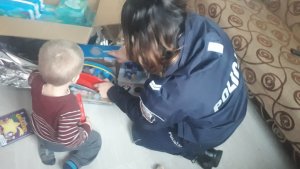 Policjantka pomaga chłopcu rozpakować część prezentu - zabawkę z ulubionym bohaterem z bajki.
