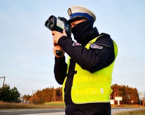 Policjant sprawdza prędkość jadących pojazdów za pomocą ręcznego miernika pomiaru prędkości