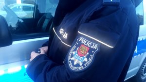 logo Komendy Powiatowej Policji w Sokółce na rękawie munduru, w tle radiowóz