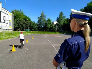 policjantka w tle dziecko jadące rowerem na boisku szkolnym