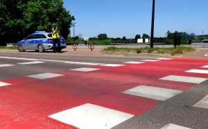 przejście dla pieszych na dalszym planie policjant mierzący prędkość pojazdów obok radiowóz