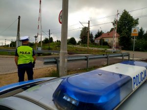 policjant obok przejazd kolejowy, na pierwszym planie lampa błyskowa radiowozu