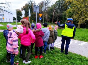 policjantka przeprowadza grupę dzieci przez przejście dla pieszych na miasteczku ruchu drogowego