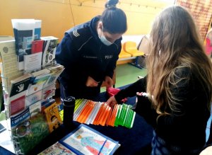 policjantka przed nią inna kobieta sięga po materiały edukacyjne ulotki i odblaski