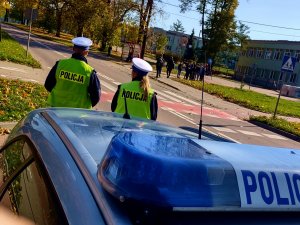 radiowóz przed nim dwoje policjantów w tle przejście dla pieszych