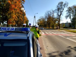 radiowóz przed nim dwoje policjantów w tle przejście dla pieszych