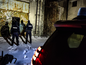 dwóch policjantów wchodzi do pustostanu na pierwszym planie reflektor radiowozu