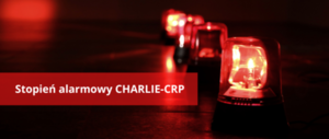 Z prawej stronie czerwone światła błyskowe, na środku na czerwonym tle  biały napis Stopień alarmowy CHARLIE–CRP .