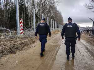 Policjanci patrolujący wzdłuż budowanej zapory na granicy. Z lewej strony widoczny słupek graniczny.