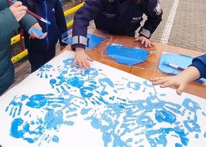 Policjantka odbija dłoń na kształt niebieskiego motyla w trakcie obchodów Światowego Dnia Autyzmu.