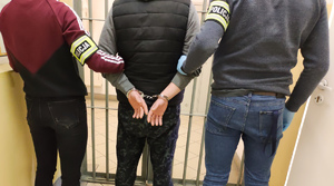 Mężczyzna w kajdankach trzymany przez policjantów.