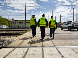 Policjant i funkcjonariusz straży kolei sprawdzają bezpieczeństwo przy przejeździe kolejowym.