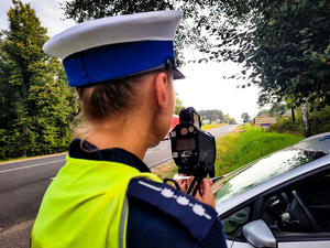 Policjantka urządzeniem do pomiaru prędkości mierzy prędkość samochodów.