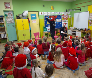 Policjantki w czapkach mikołaja rozmawiają z przedszkolakami.
