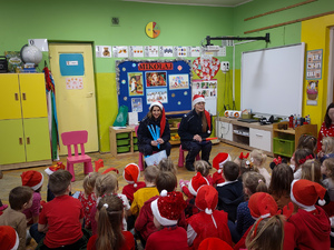 Policjantki w czapkach mikołaja rozmawiają z przedszkolakami.