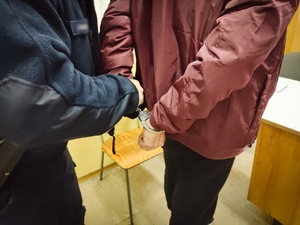 Policjant zakłada mężczyźnie kajdanki na ręce trzymane z tyłu.