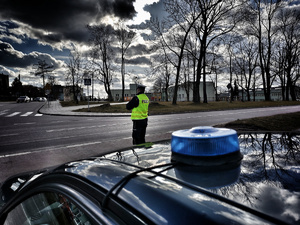 Policjant przy drodze, na pierwszym planie światło błyskowe.