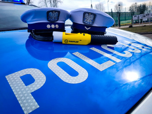 Czapki policjantów ruchu drogowego i urządzenie do badania trzeźwości na masce radiowozu.
