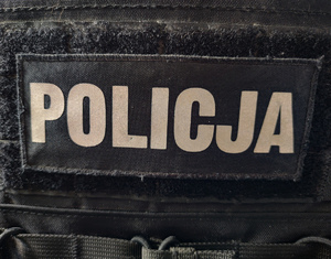 Biały napis policja na czarnej kamizelce.