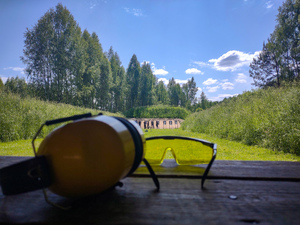 Słuchawki i okulary leżą na stole. W oddali strzelnica.