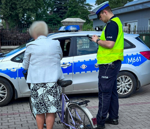 Policjant rozmawia z rowerzystką, za nimi radiowóz.