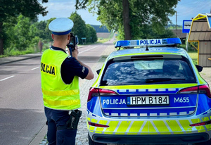 policjant mierzy prędkość, obok stoi radiowóz