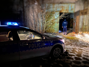 Radiowóz, w oddali policjant sprawdzający pustostan.