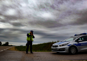 Policjant mierzy prędkość pojazdów, obok radiowóz.