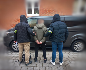 dwóch policjantów z zatrzymanym mężczyzną.
