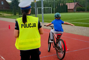 Policjantka w białej czapce, obok dziecko na rowerze wykonuje slalom.