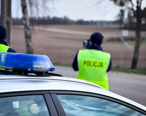 Policjant mierzy prędkość pojazdów obok radiowóz.