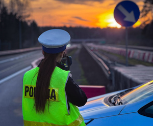 Policjantka mierzy prędkość pojazdu, w oddali zachód słońca.